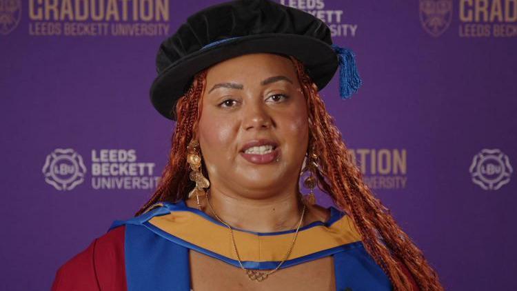 Emily Campbell, Olympic weightlifter, in a cap and gown as she receives an honorary doctorate. She stands in front of a purple background.