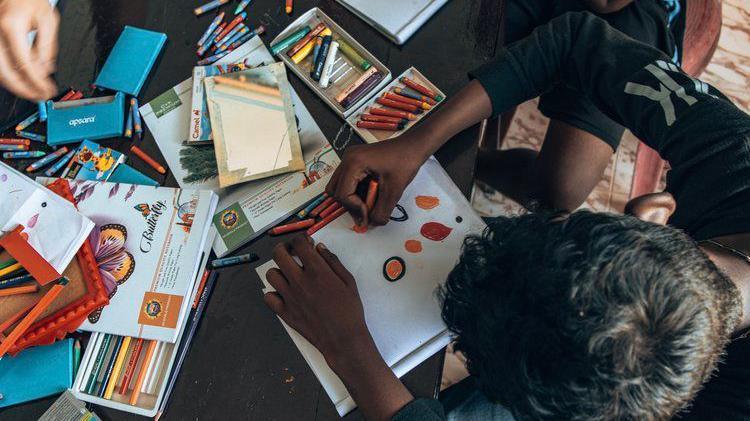 A Birds eye view of children drawing shapes and colours at a table full of stationary and paper