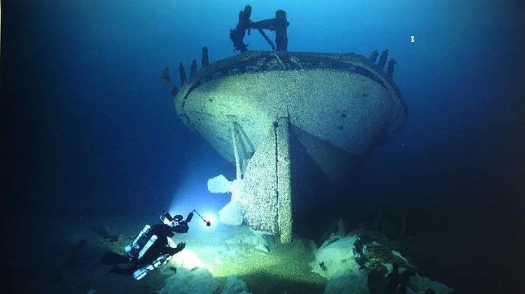 A diver with a light looks at the ships hull under water