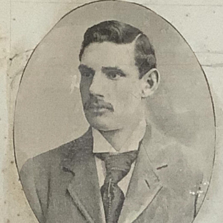 A black and white photograph of Ernest William Taylor.  He is wearing a dark suit and a large-knotted tie. He has a moustache and dark hair parted at the side.