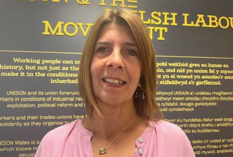 Rosie Lewis smiles at the camera. She has shoulder-length straight auburn hair and earrings in the shape of a star. She is wearing a pink shirt.
