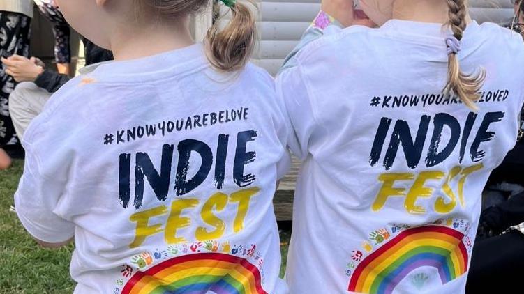 Two young children with their backs to the camera wearing T-shirts branded with 'IndieFest'. They carry the hashtag know you are be loved