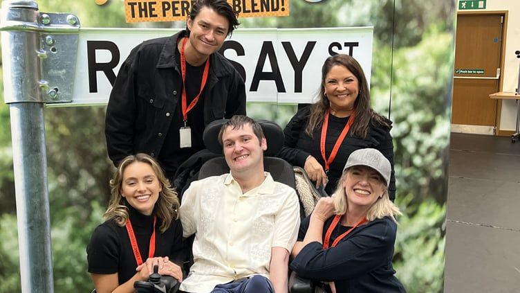 Alex Christmas with members of the Neighbours cast next to a Neighbours sign