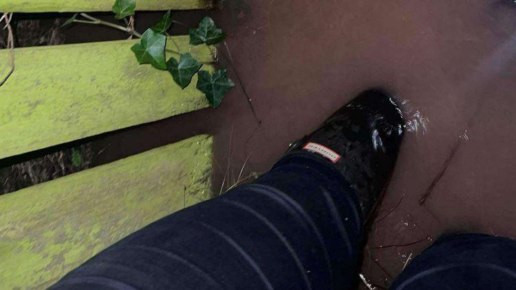 Flood water is shown rising up a person's Wellington boots in a garden