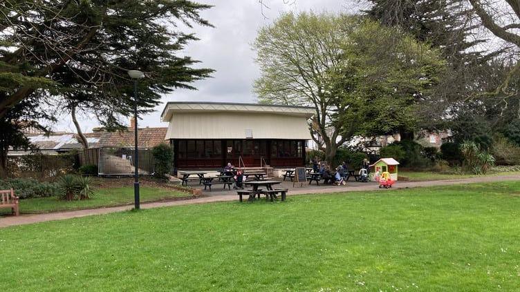 A cafe building with picnic tables outside set in a park with grass and trees surrounding it