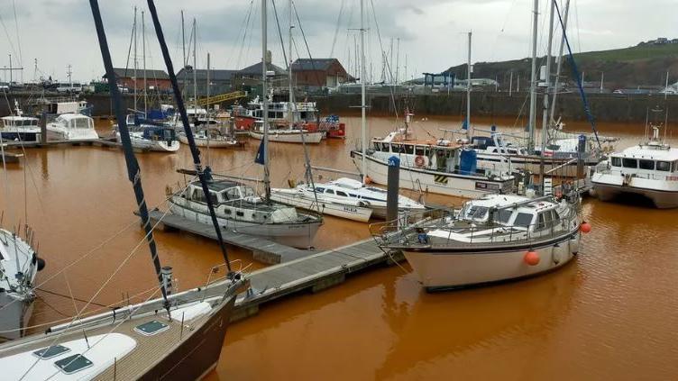 A general view of Whitehaven Harbour with brown water surrounding the boats