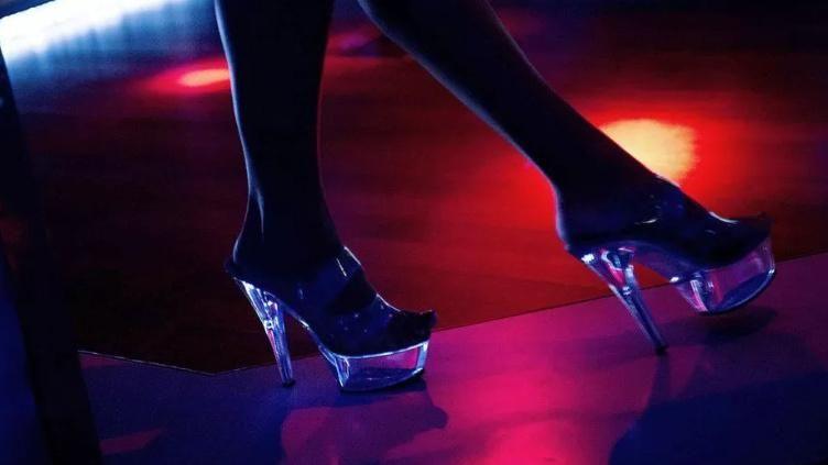 Stock image of a woman's legs and feet. She is wearing high heels and appears to be in a late night venue.