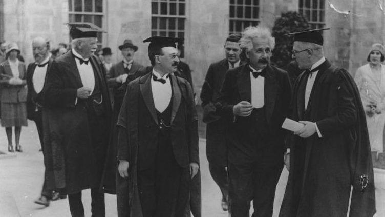 A picture of Albert Einstein at the University of Nottingham talking to two men in suits.