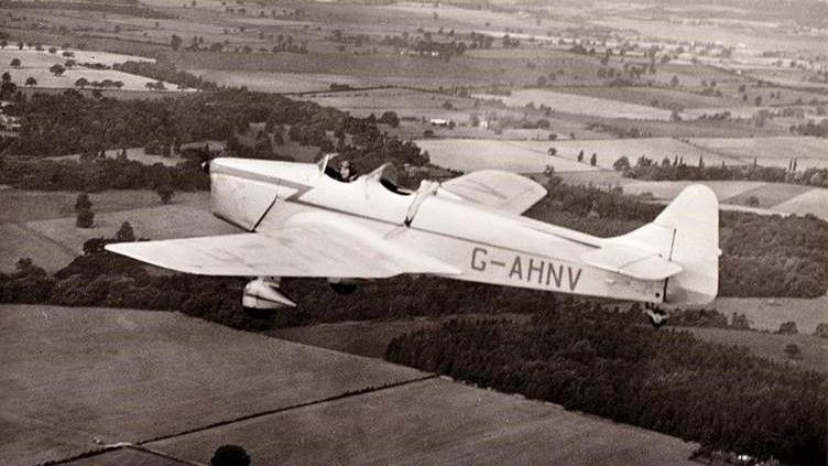 An archive photograph of a Wellington Bomber flying over the countryside. The aircraft is above fields and trees around Croome Court.