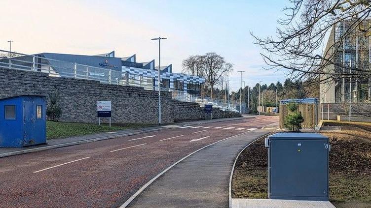 The road leading into Hydebank test centre. There is a zebra crossing and two buildings either side of the road