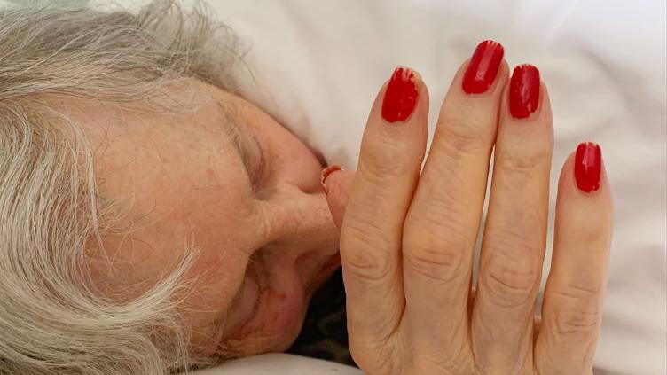 Vivian lies in bed with her hand close to her face. Her nails are painted red.