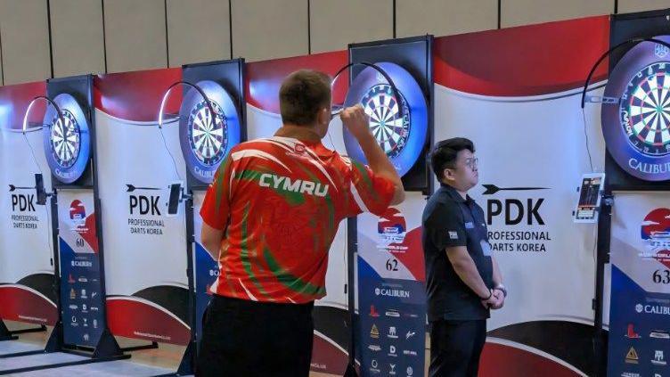 David Davies in a Wales darts shirt throwing darts at a dart board