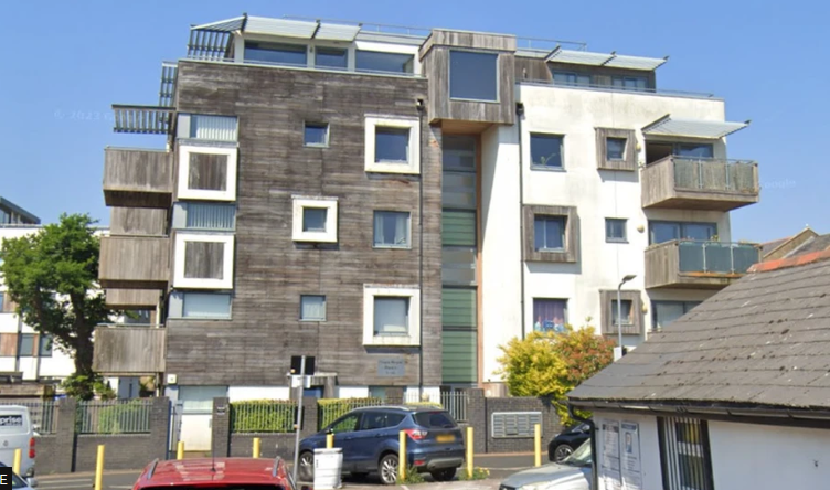 A modern-day block of flats of about five storeys. It has wooden cladding on the exterior and each flat has a wooden-clad balcony.