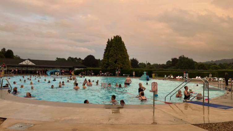 Hundreds of swimmers in the outdoor pool at dusk