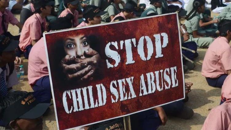 Children sit in protest and hold a 'Stop child sexual abuse' sign