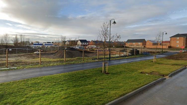 A building site where the proposed nursery and shop could be built. It has a large pile of mud in the middle, is fenced off and is next to a road that leads to houses.