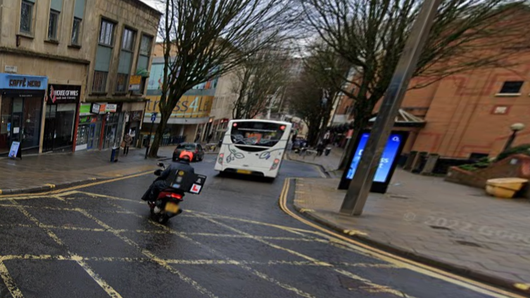 A view looking down Union Street in Bristol with a moped rider and bus visible