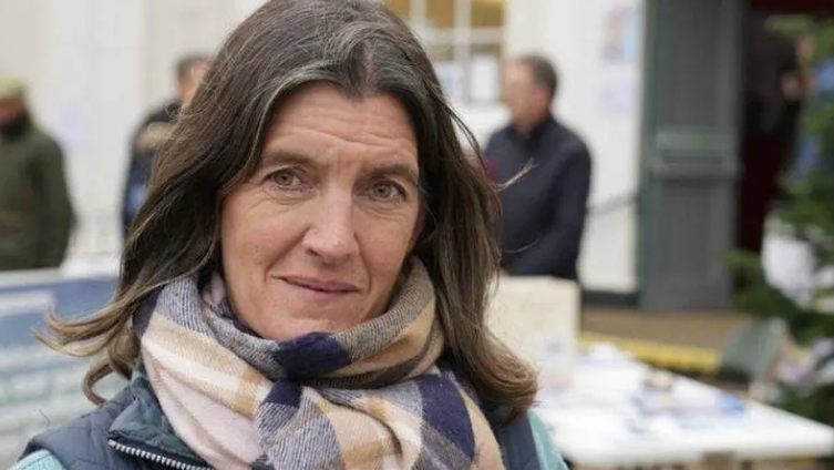 Rosie Pearson with mid-length brown hair looks into the camera. She is wearing a scarf with a purple, beige and pink checked pattern.