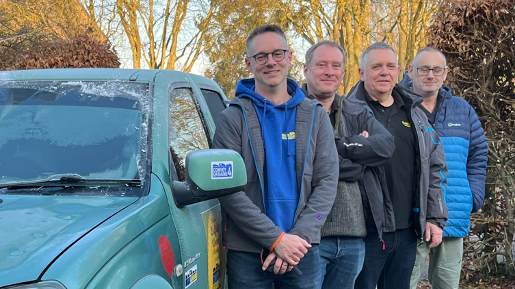 Four men, Alistair Gray, Paul Earnshaw, Fergus Ramsay and Craig Wrightson, are standing next to a green 4x4 humanitarian air car which has frost on the windows. The men are smiling at the camera and are wearing coats. 