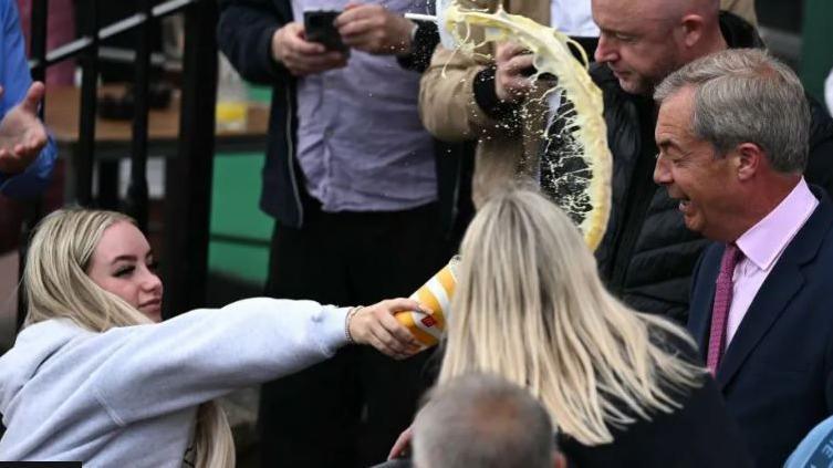 A woman in a crowd throwing milkshake towards Nigel Farage