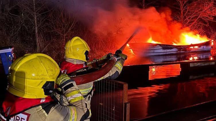 Two firefighters try to put out a burning pleasure boat