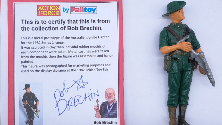 An 'Australian Jungle Fighter' figure of a man with a green hat and suit carrying a gun is displayed next to a certificate of authenticity featuring Bob Brechin's photograph and signature.