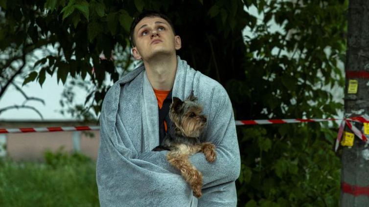 A resident holds his dog as he looks an apartment building that was damaged during a Russian drone strike in the Ukrainian capital Kyiv