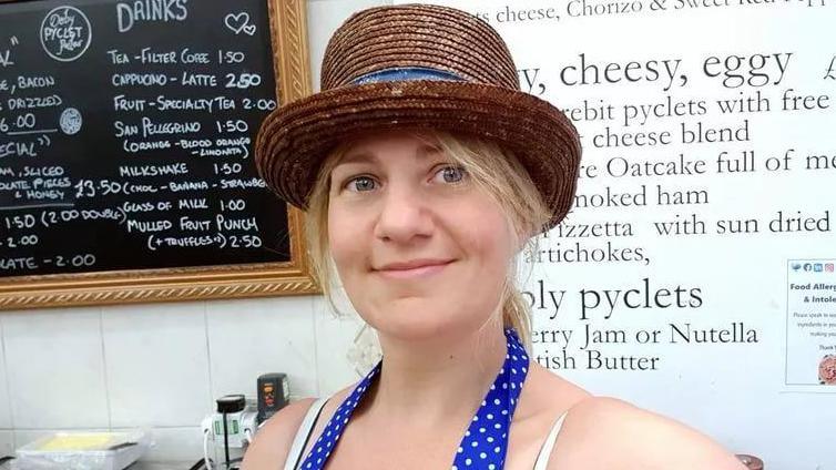 Katie Gibson, who has blonde hair and blue eyes, wearing a hat and blue apron