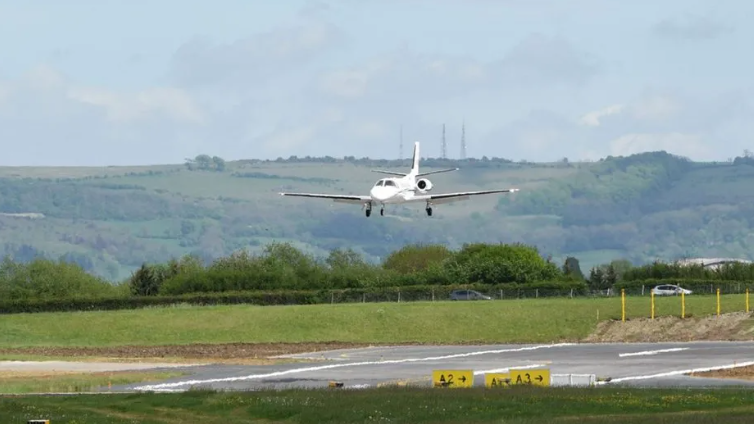 A plane comes into land at Gloucestershire Airport, with trees and hills in the background. 