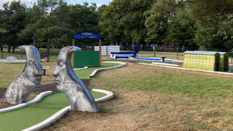 The crazy golf course featuring the Faces statue, airship hangars, a market stall, a boat and a bridge