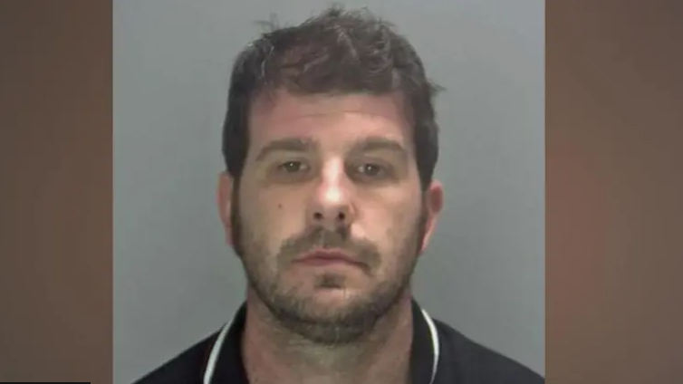 Head and shoulders police mugshot image of Stuart Worby in a black polo shirt with white trim around the edge of the collar. He has short dark hair and dark stubble and is expressionless as he looks at the camera.