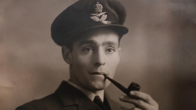 A black and white photograph featuring Roy Daines as a young man in military uniform. He has a smoking pipe in his mouth and he is looking past the camera.