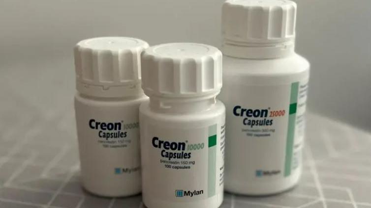 Three bottles of Creon capsules on a grey surface