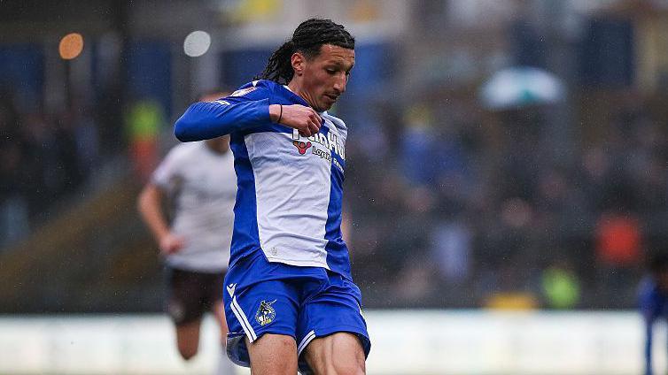 Yusuf Akhamrich in royal blue and white Bristol Roves kit looks down to control the ball