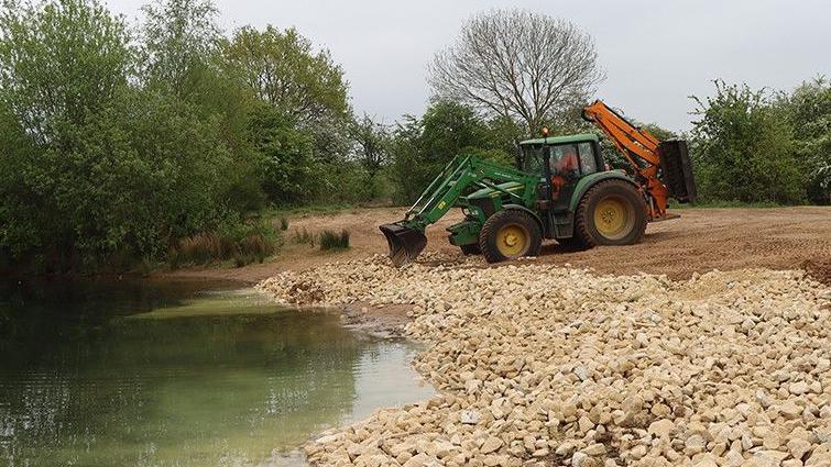 digger laying stones at waterside