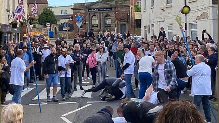 Two people fighting on the ground as a crowd looks on