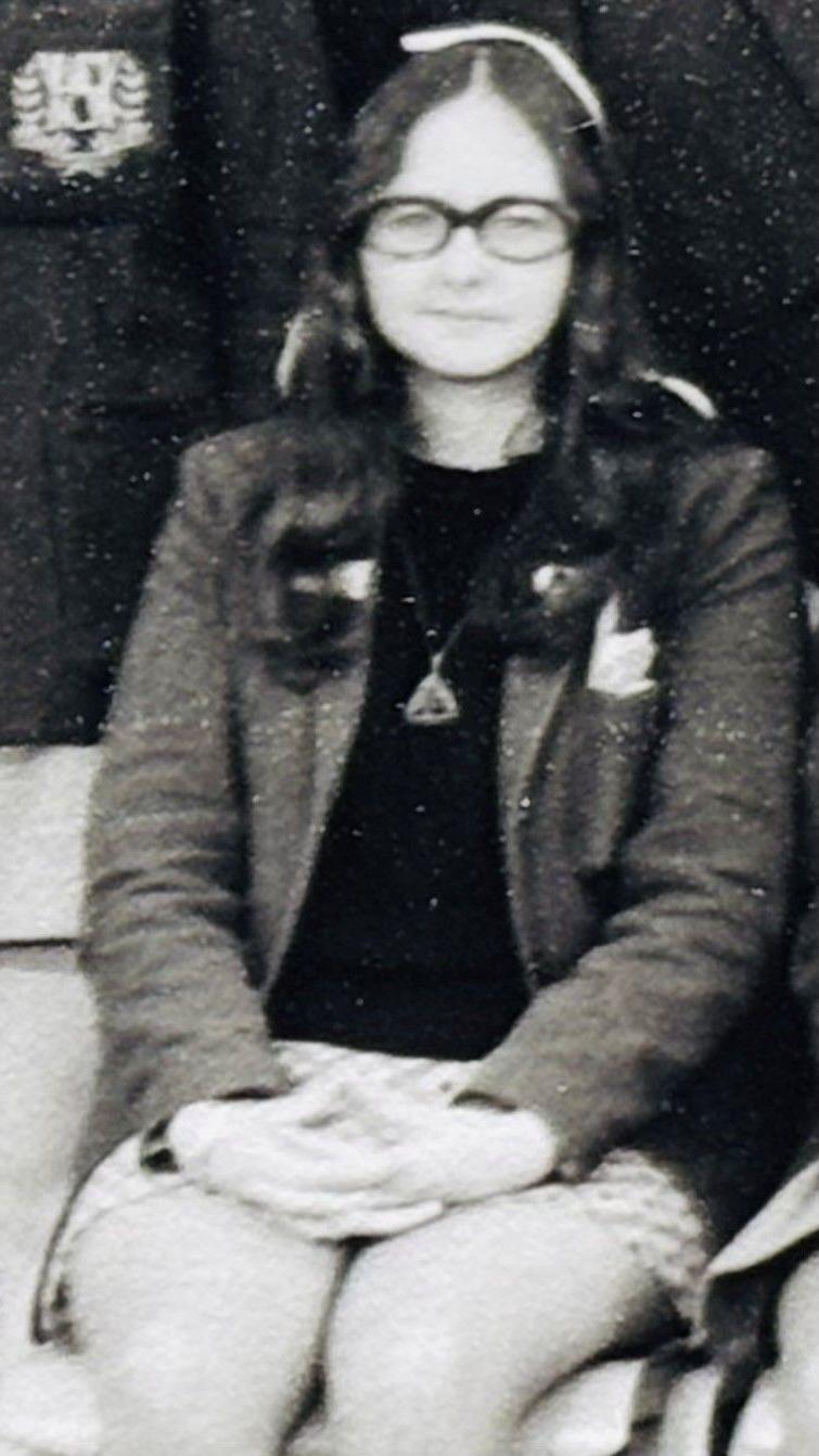 Black and white photo of Liz Slaven as a schoolgirl in uniform looking at camera in a class photo.
