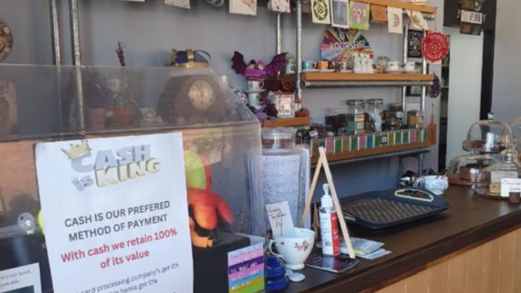 A cafe counter with a sign saying "Cash is king". A shelf with teapots on is in the background.