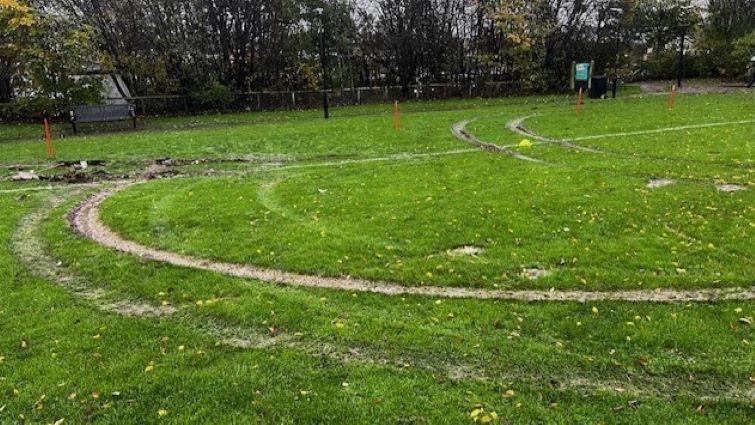 A football pitch with large tyre tracks all over the grass, wrecking it.
