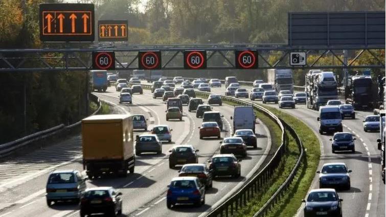 Traffic move in both directions on a busy smart motorway section of road. 