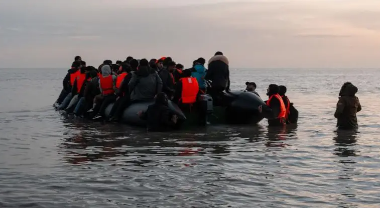 A group of migrants pictured in a dinghy crossing the English channel. A few individuals are stood up in the water.