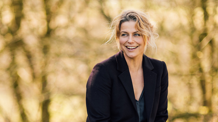 Tanya smiling in black jacked with tress behind her