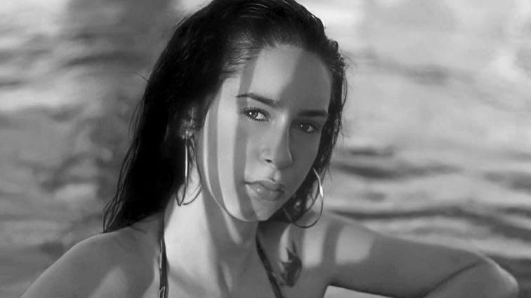 A black and white photo of Sofia Duarte wearing a swim suit and looking at the camera. She has dark hair down to her shoulders and large hooped earrings