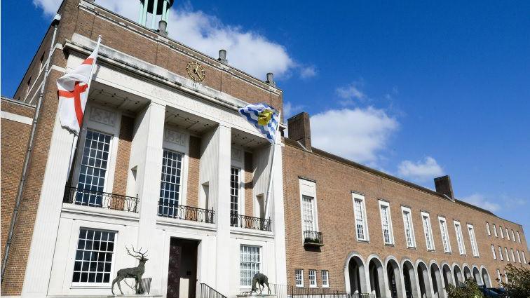 A picture of Hertfordshire county council's offices in Hertford. It is an old style brown brick building with white bits, and there is blue sky behind the building.