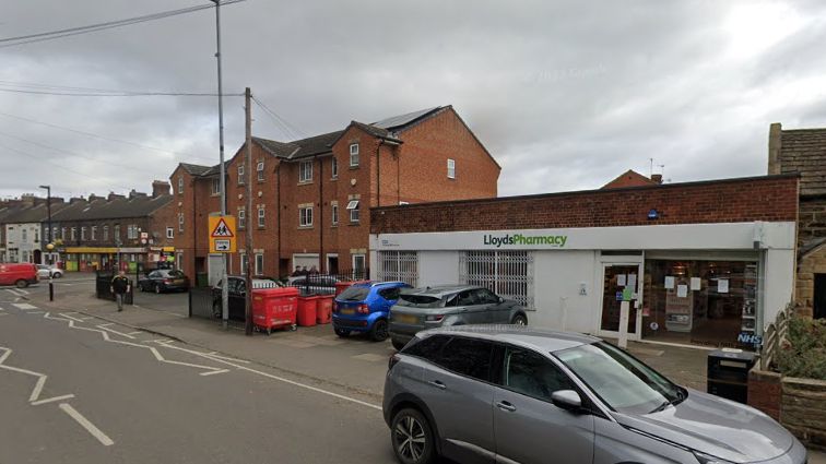 A semi-residential street with a pharmacy and a number of parked cars
