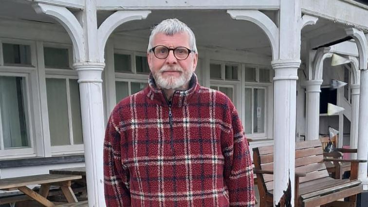 Steve Wordley wears a red tartan fleece and glasses, looking into the camera while standing outside the building.