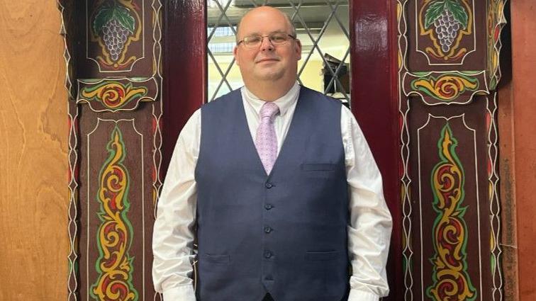 Museum director Edward Fagan, dressed in a suit and tie, wearing glasses, stands outside a decorative doorway 