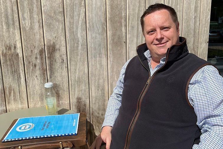 Reform candidate Phil Walton sitting on a chair with his election papers in front of him. He's wearing a checked shirt and a black gilet. 