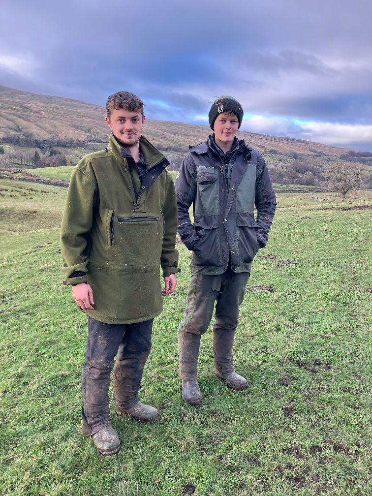 Luke and Lewis wearing outdoor farming gear and wrapped up warm. They are standing in a field