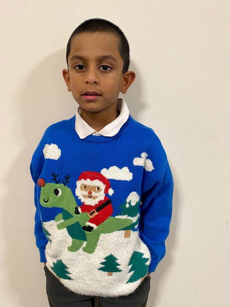 boy in a christmas jumper showing santa riding a dinosaur